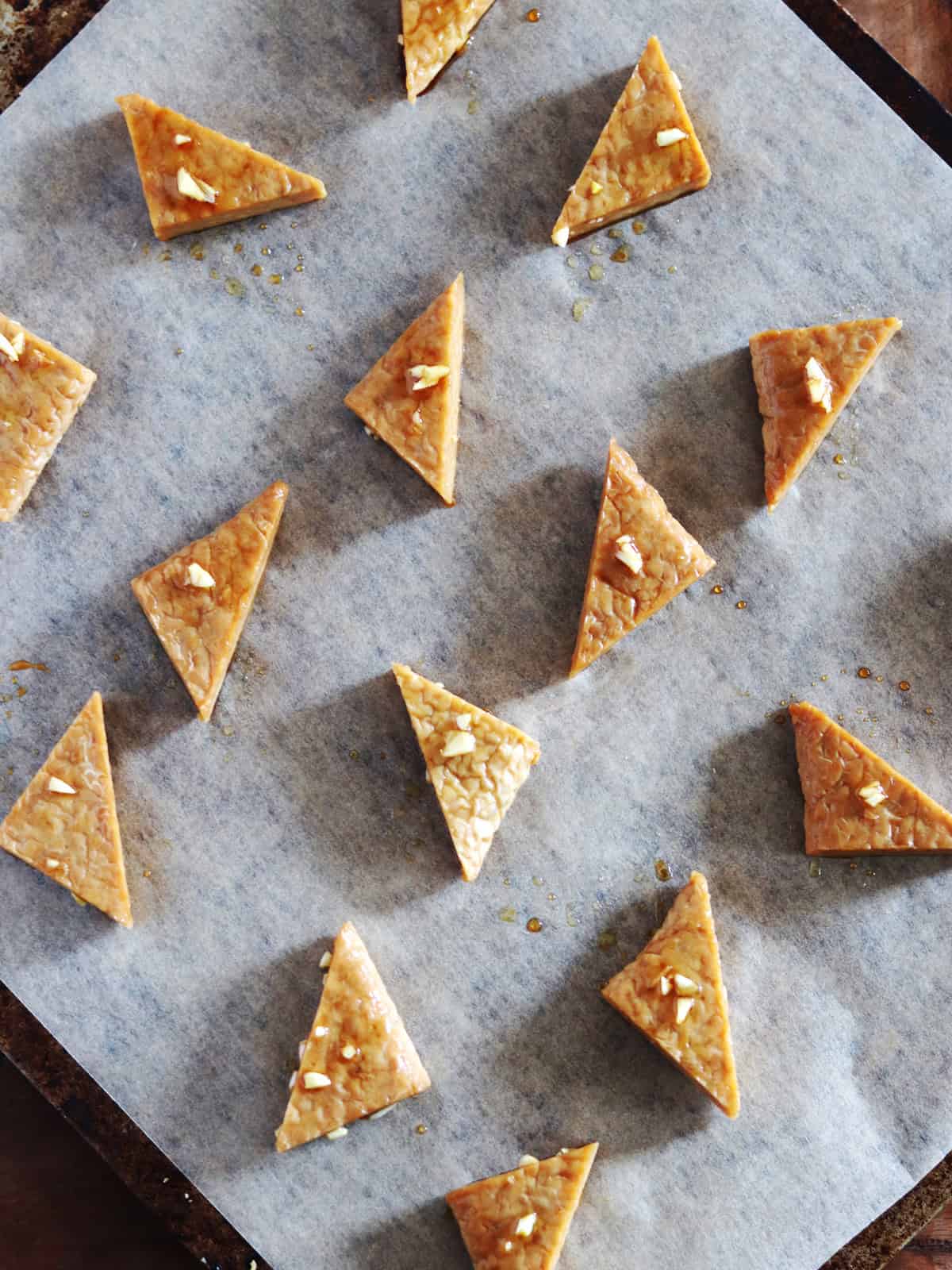 Marinated tempeh triangles arranged on a parchment paper lined baking sheet.