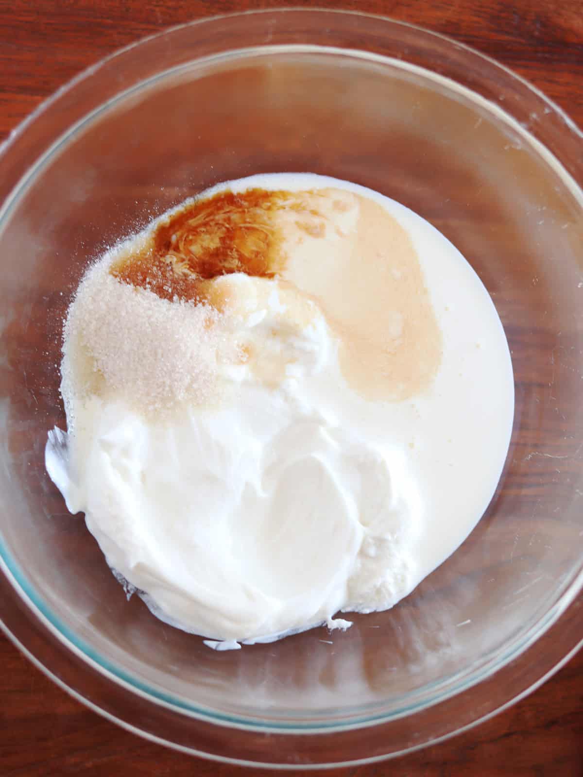 Greek yogurt, heavy cream, granulated sugar and vanilla extract in a large glass mixing bowl.