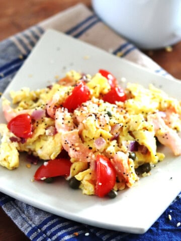 Scrambled eggs with smoked salmon on a square ceramic tan plate.