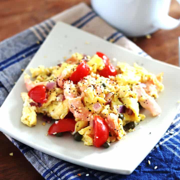 Scrambled eggs with smoked salmon on a square ceramic tan plate.