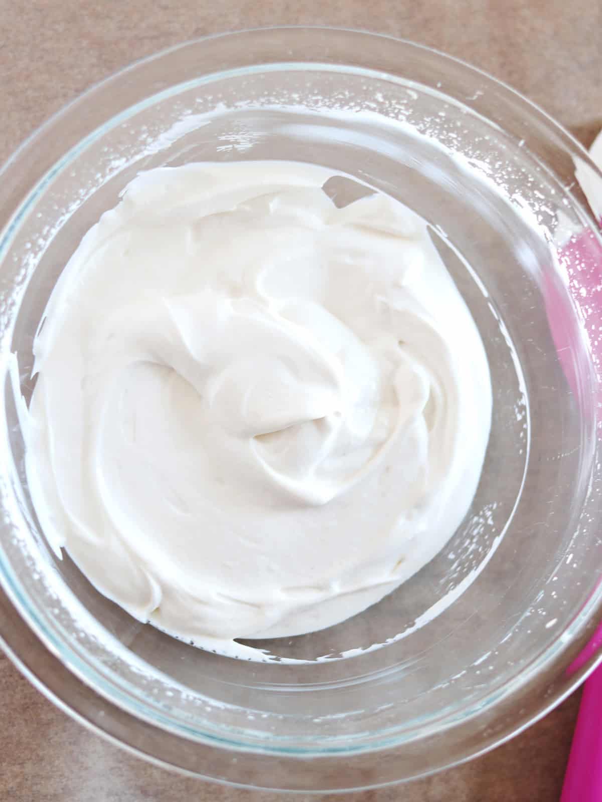 Whipped Greek yogurt with soft peaks in a glass mixing bowl.