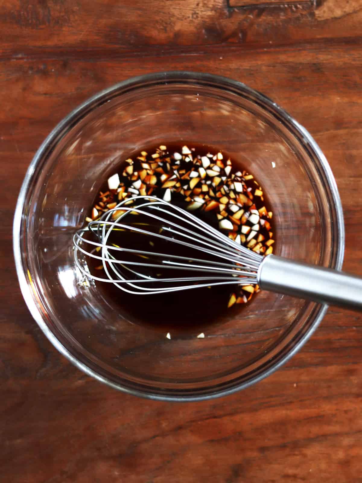 Tamari, maple syrup and fresh garlic marinade in a glass bowl with a stainless steel whisk.