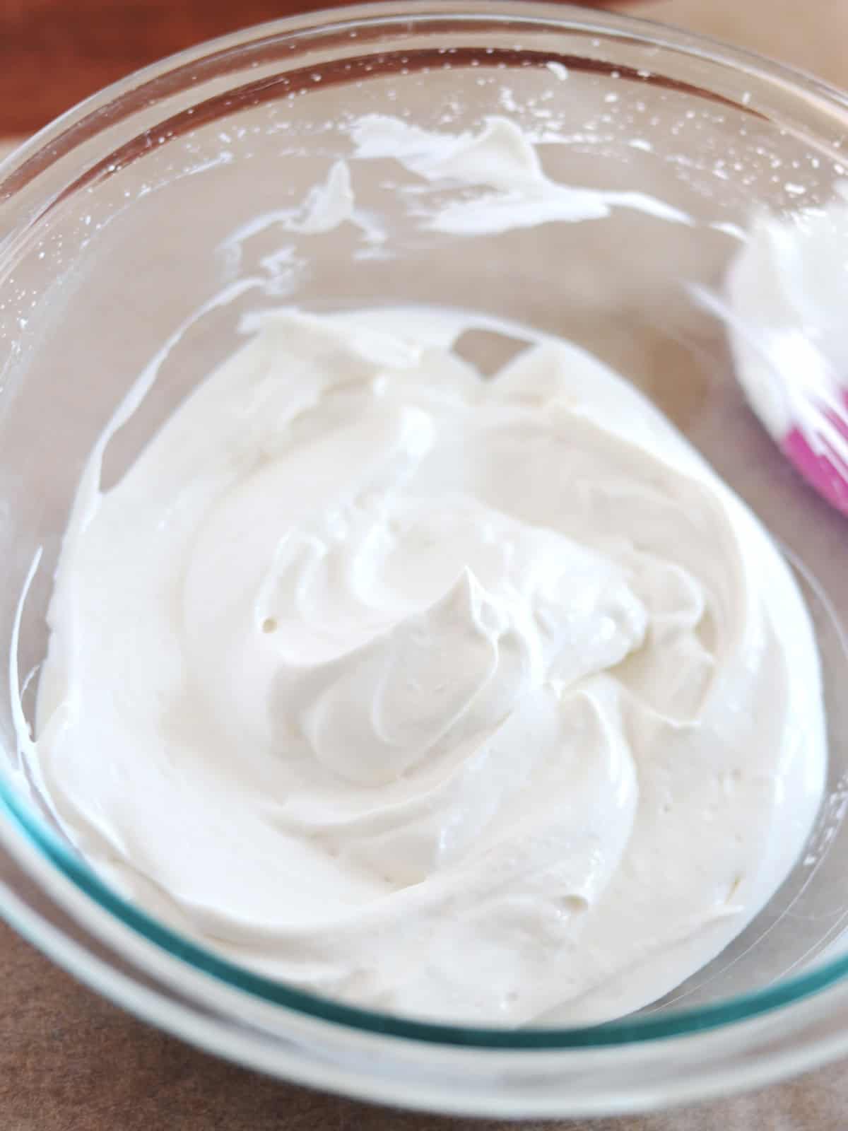 Whipped Greek yogurt in a glass mixing bowl on a parchment paper lined table.