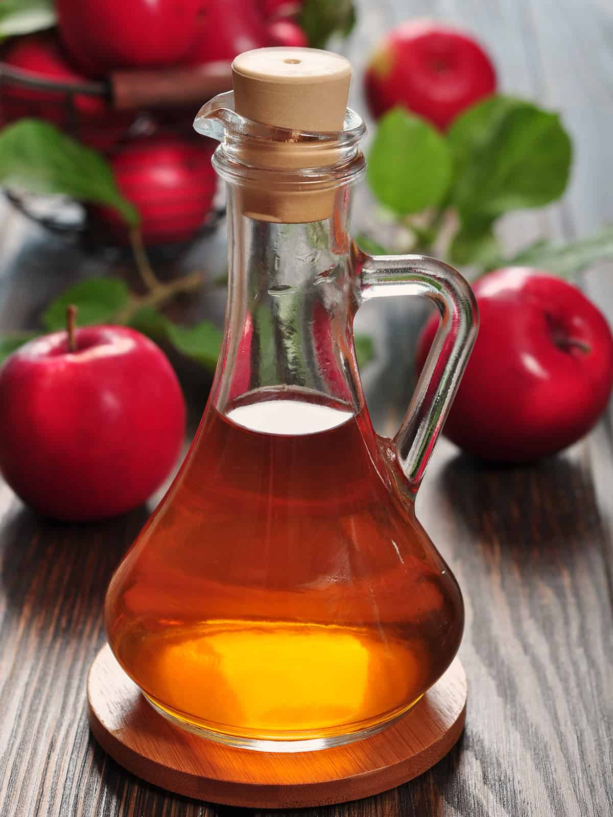 Homemade apple cider vinegar in a glass carafe with decorative red apples in the background.