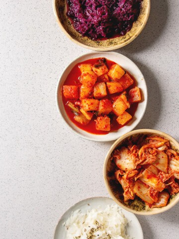 Four ceramic bowls of red and white cabbage sauerkraut, kimchi and Korean fermented vegetables.