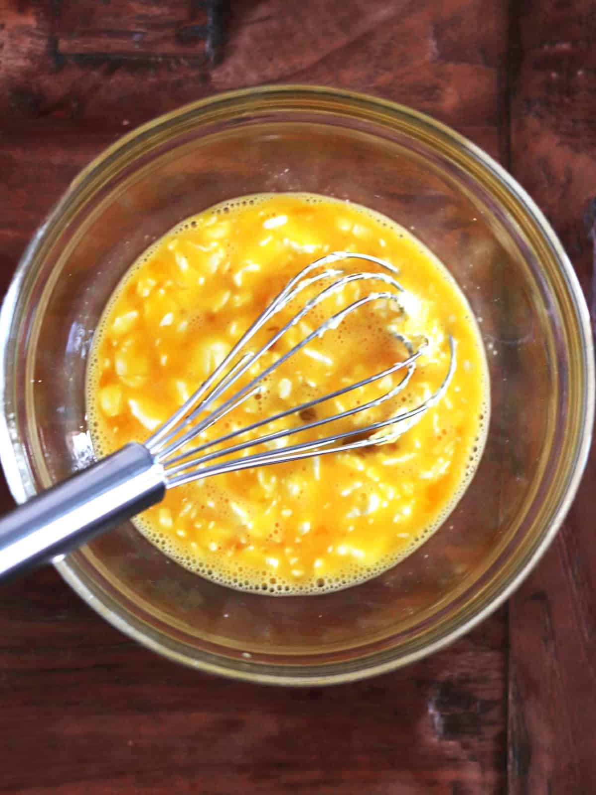 Eggs and cream cheese chunks with a whisk in a glass mixing bowl.
