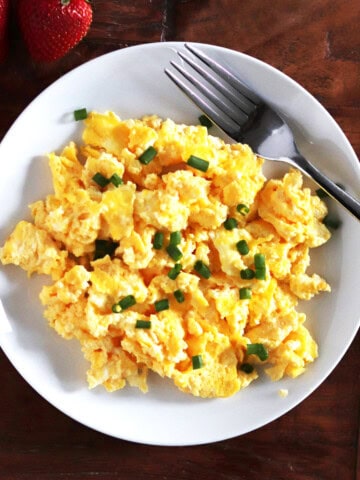 Scrambled eggs with cream cheese and chives on a white plate.