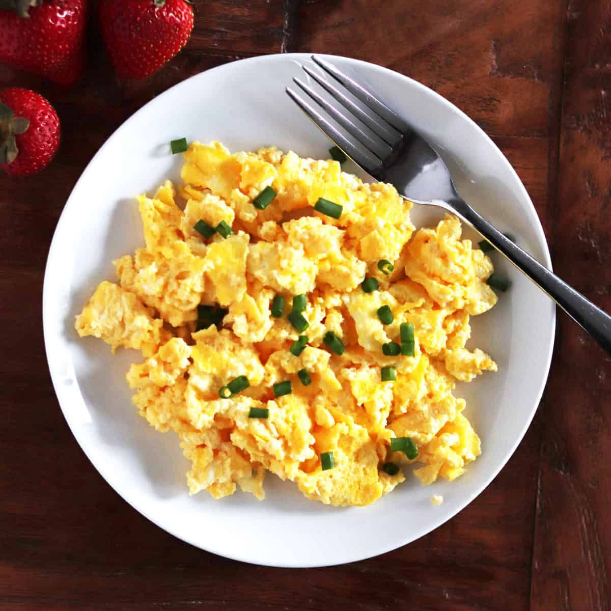Scrambled eggs with cream cheese and chives on a white plate.