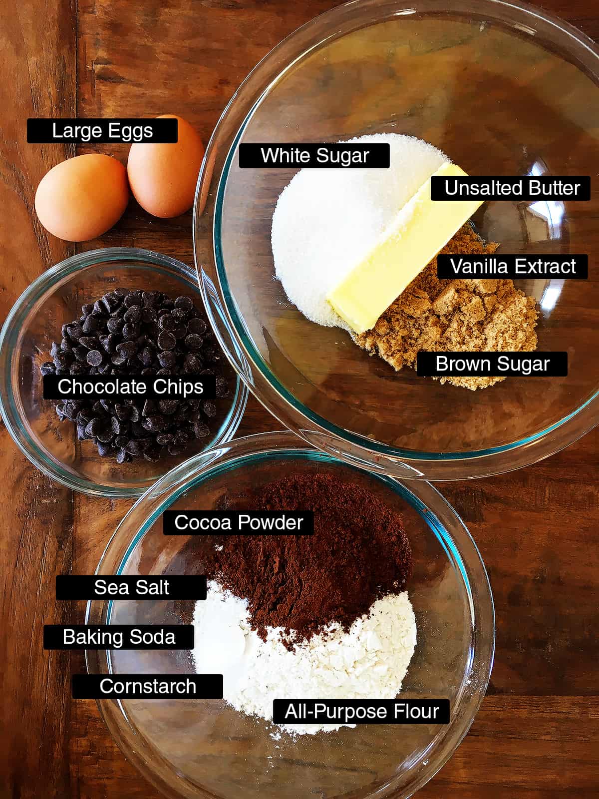 Ingredients for chewy double chocolate chip cookies arranged on a brown wood table.