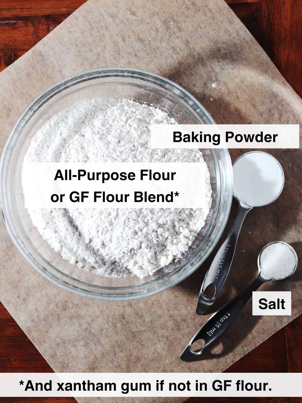 Ingredients for homemade self rising flour displayed on a parchment paper lined wood table.