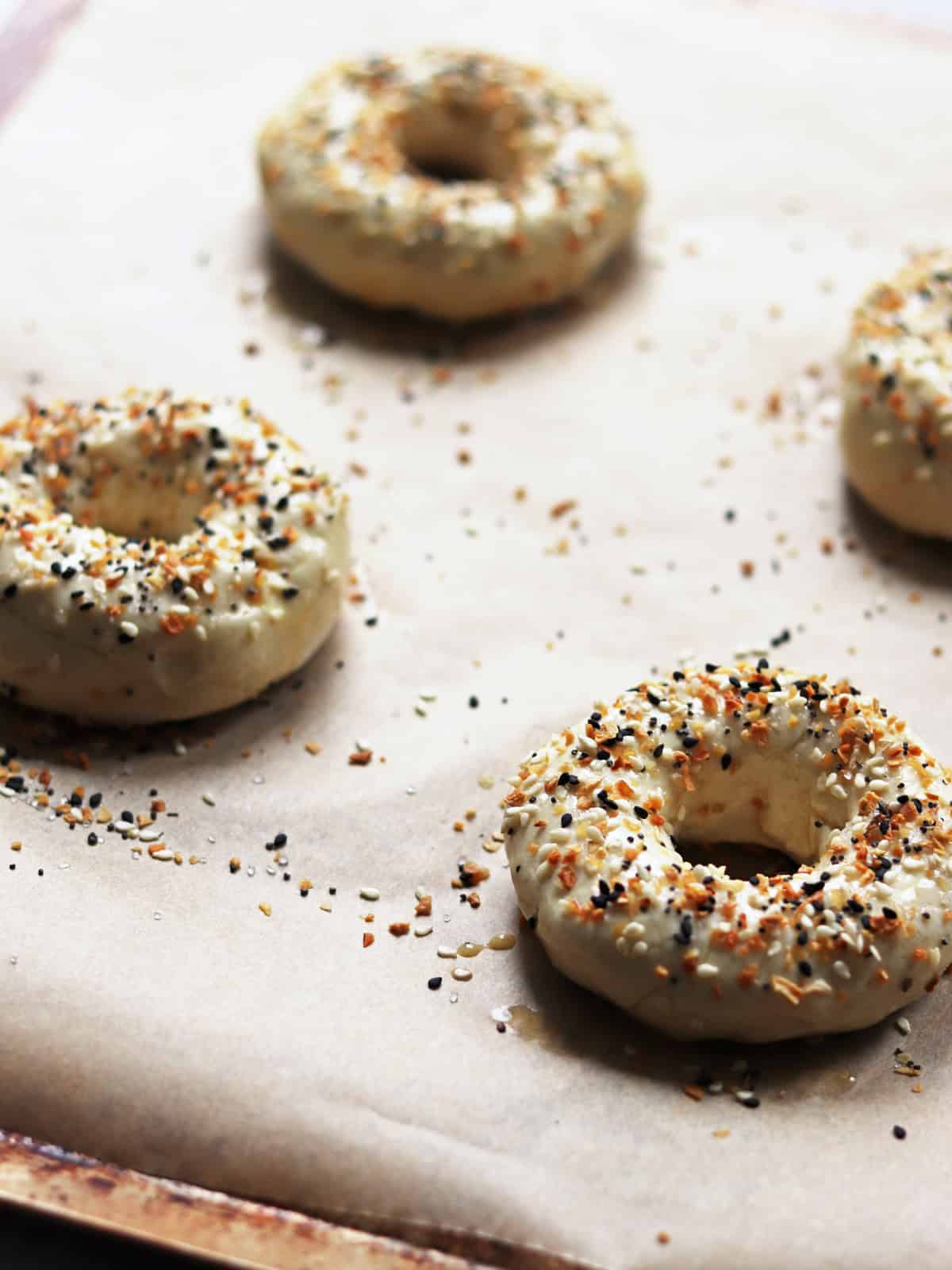 Four bagels topped with everything bagel seasoning on a parchment paper lined baking sheet.