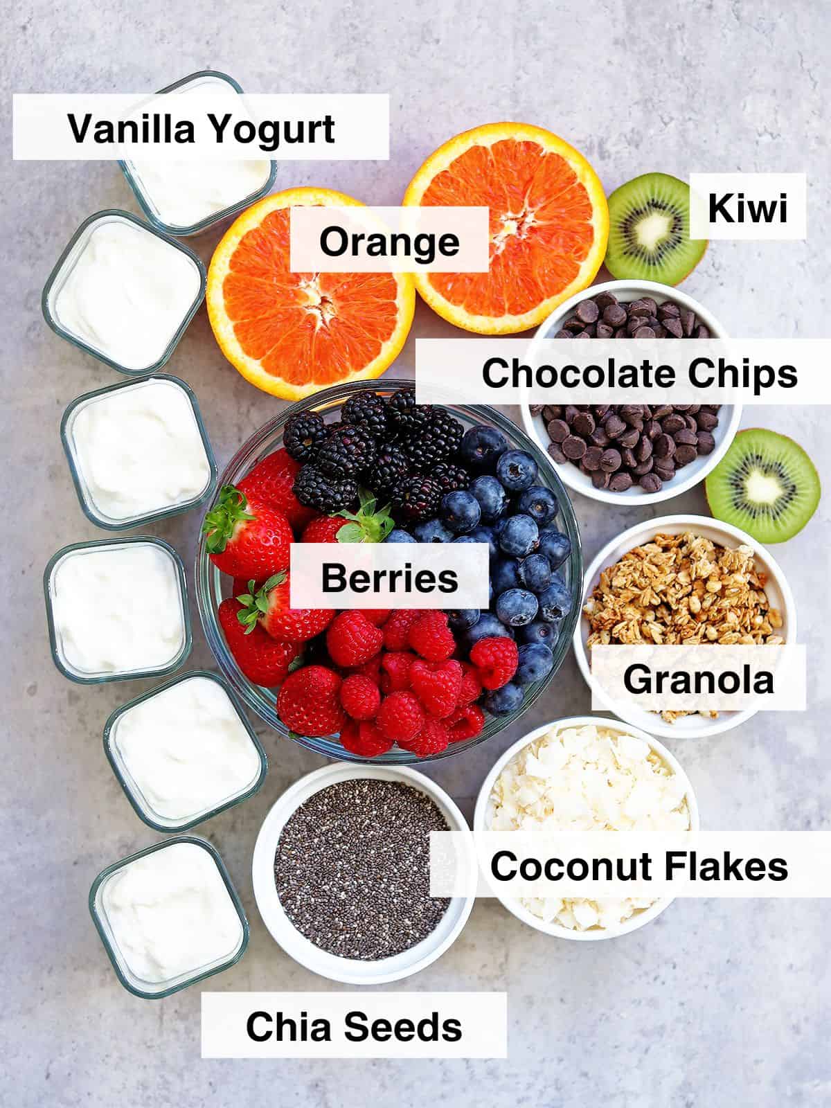 Yogurt charcuterie board ingredients in glass and ceramic dishes on a concrete countertop.