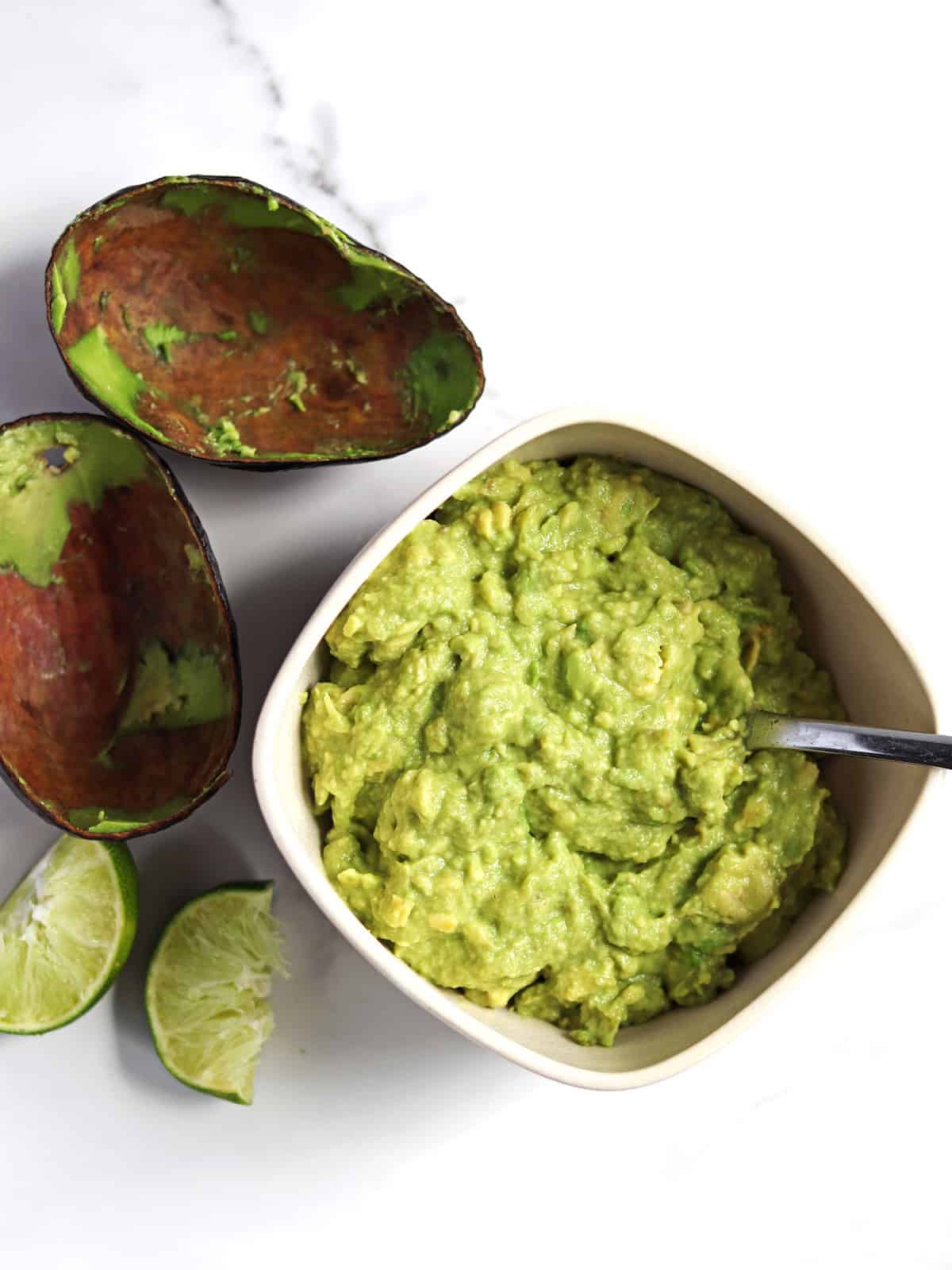 Homemade guacamole in a tan serving dish on a marble countertop.