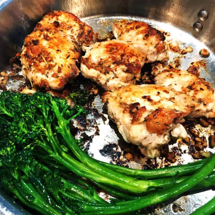 Pan seared chicken thighs and broccolini in a stainless steel skillet.
