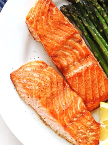 Oven baked salmon fillets on a white plate with a side of asparagus.