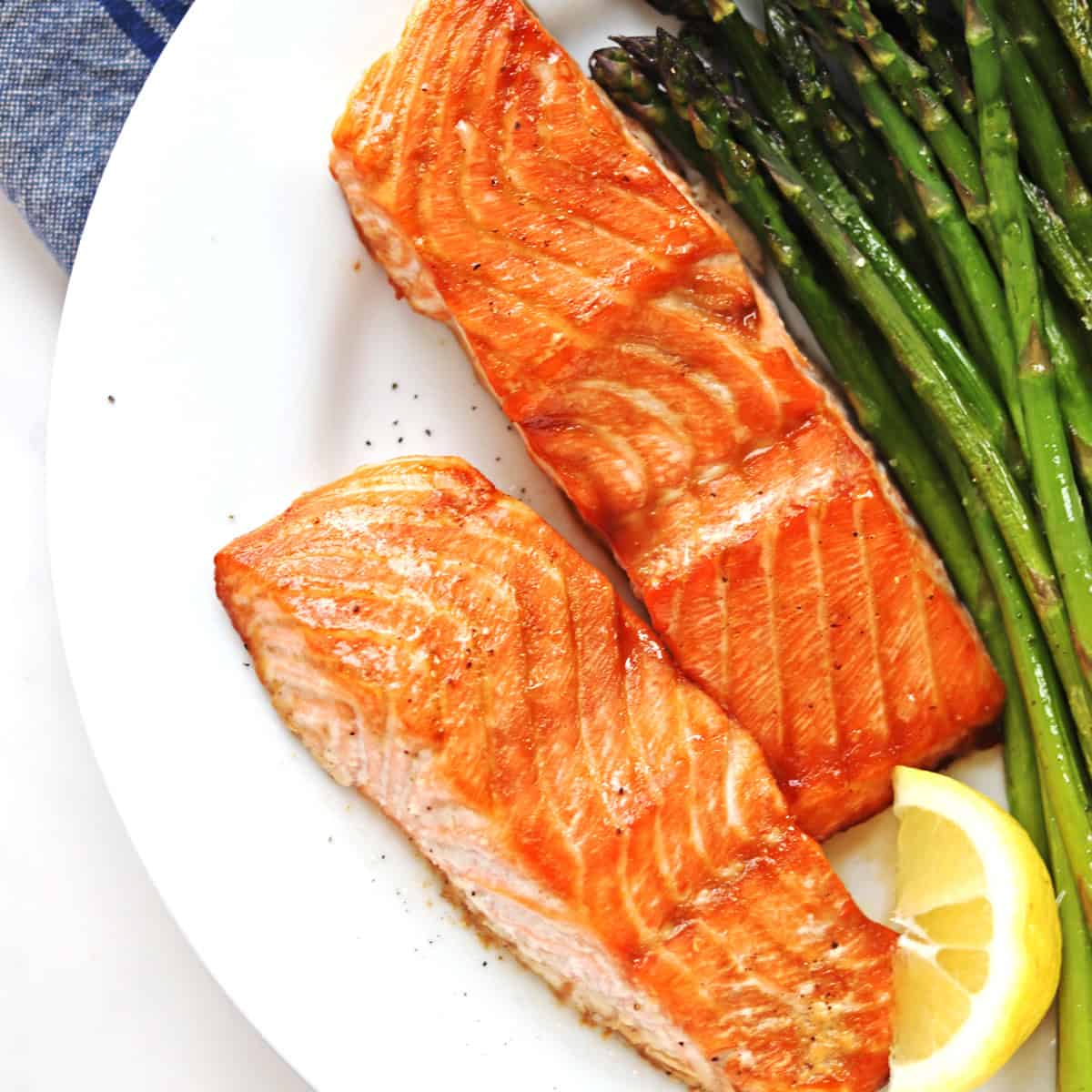 Oven baked salmon fillets on a white plate with a side of asparagus.