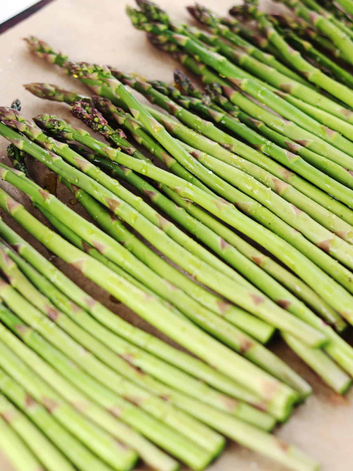 Trimmed and seasoned asparagus spears on a parchment paper lined baking sheet.