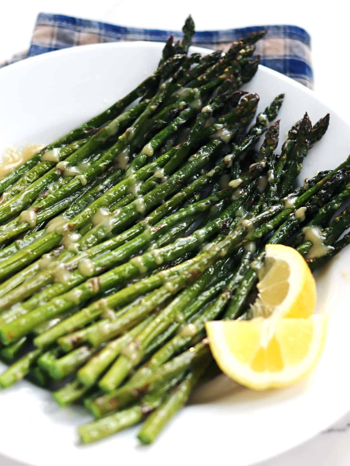 Oven roasted asparagus with maple miso glaze on a white plate with two lemon slices.