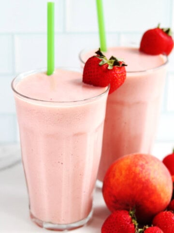 Two large strawberry peach smoothies with green straws.