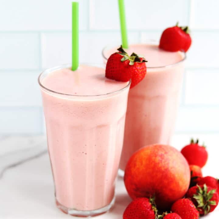 Two large strawberry peach smoothies with green straws.