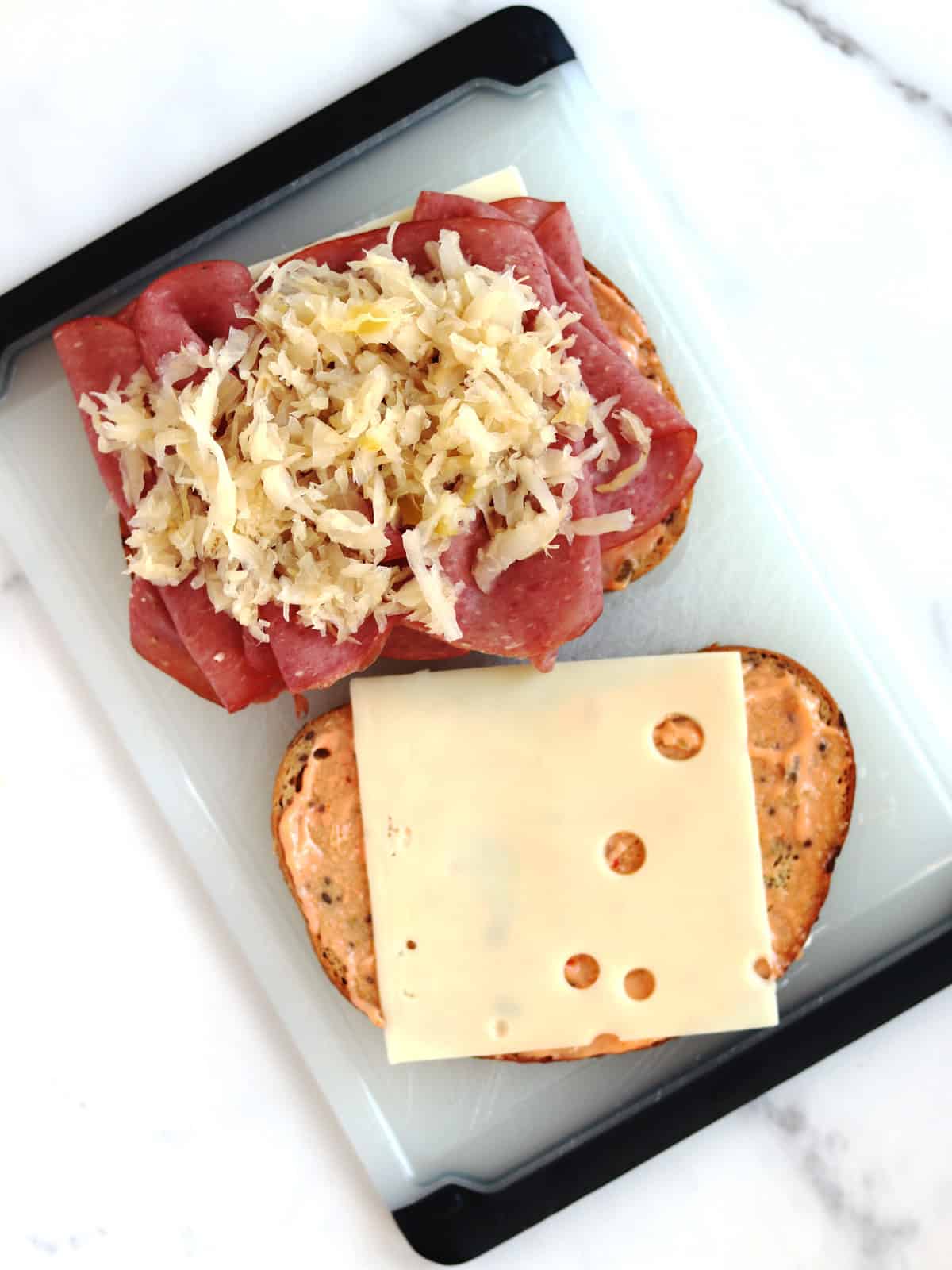 Two halves of a Reuben sandwich topped with Thousand Island dressing, Swiss cheese, corned beef and sauerkraut.