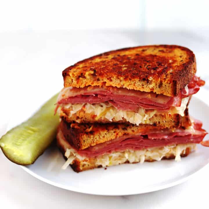 Two halves of a Reuben sandwich stacked on a white serving plate.