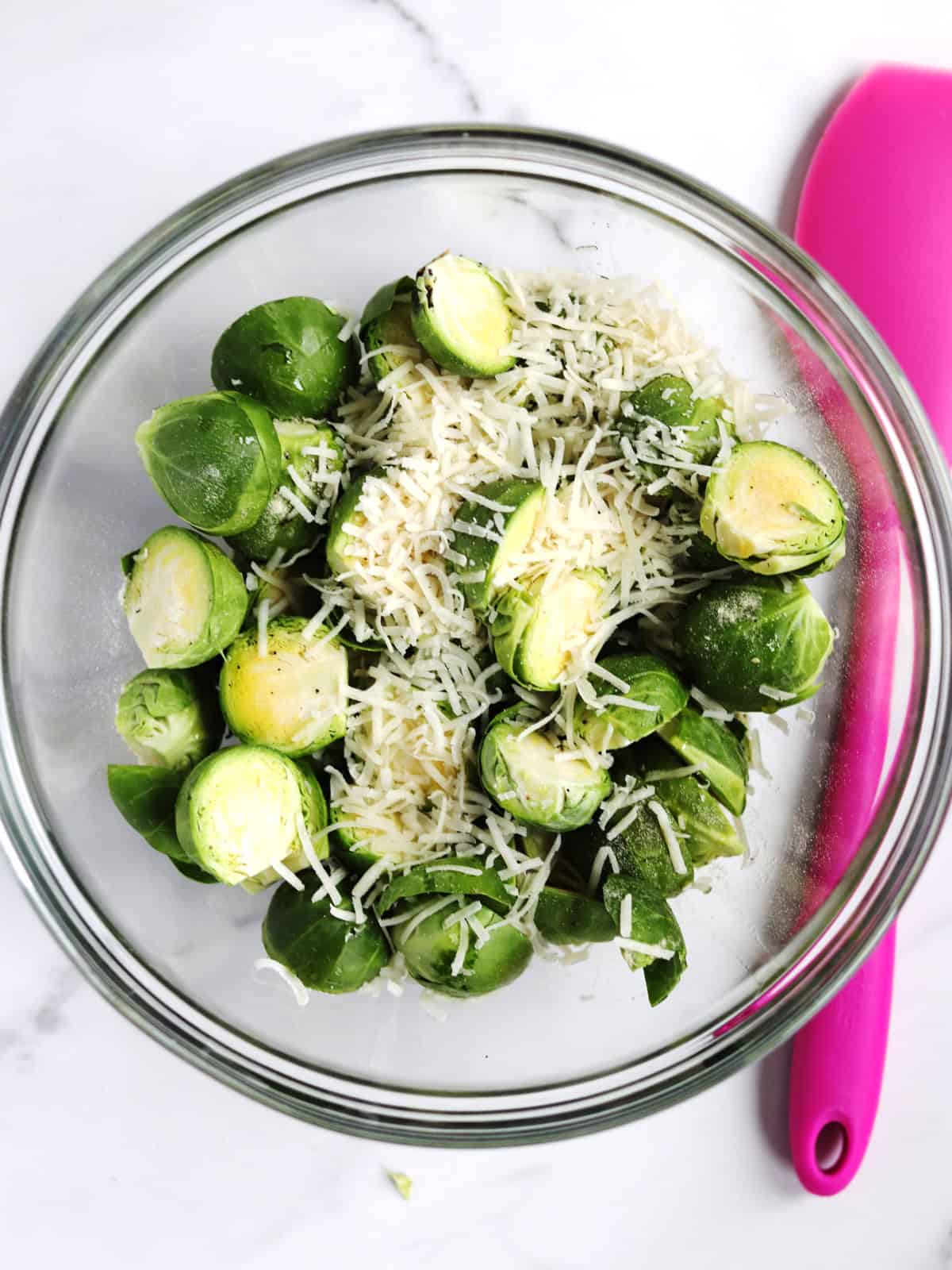 Trimmed Brussels sprouts and freshly shredded Parmesan cheese in a glass mixing bowl.