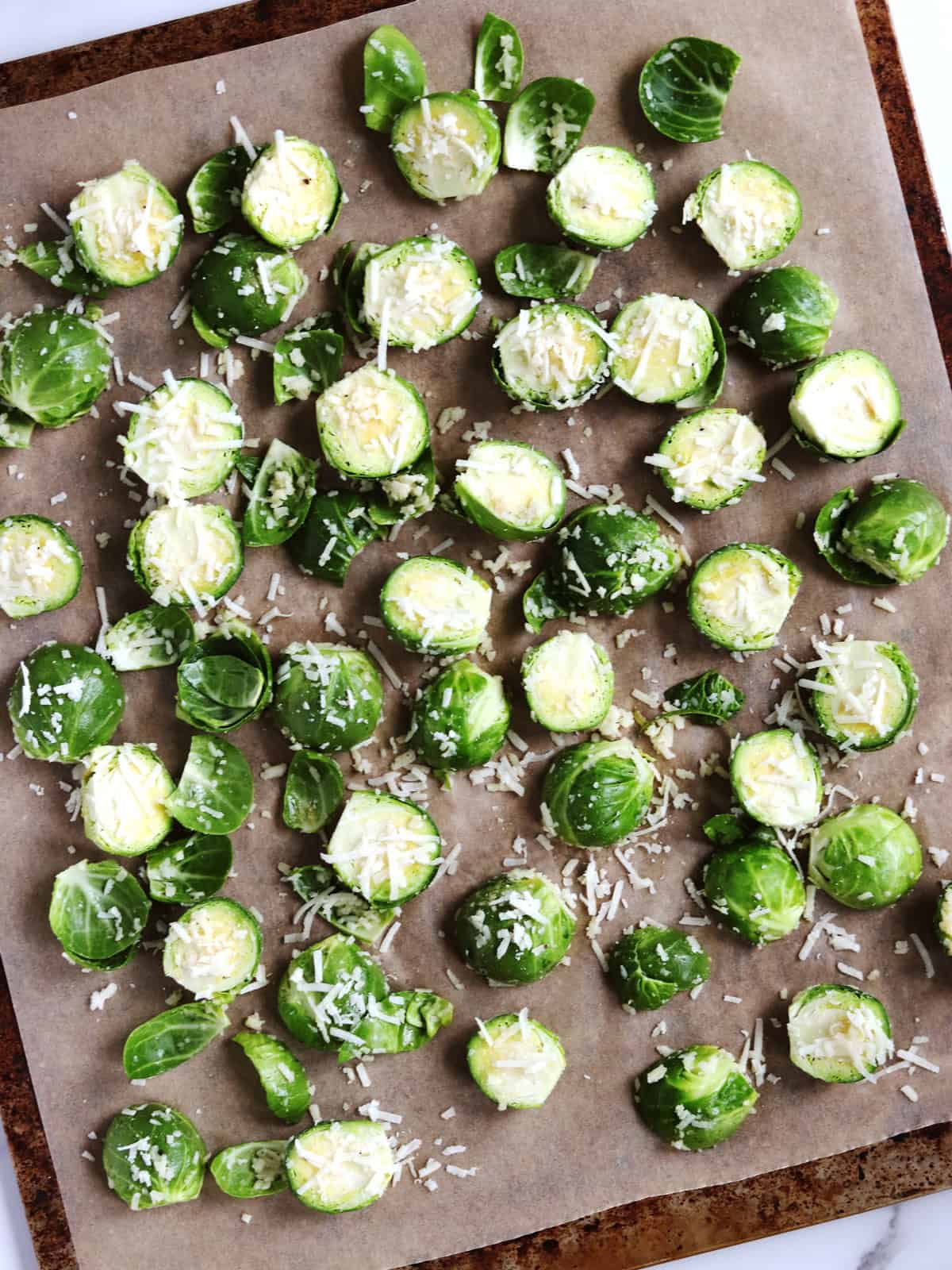 Brussels sprouts coated with olive oil, spices and shredded Parmesan on a parchment paper lined baking sheet.