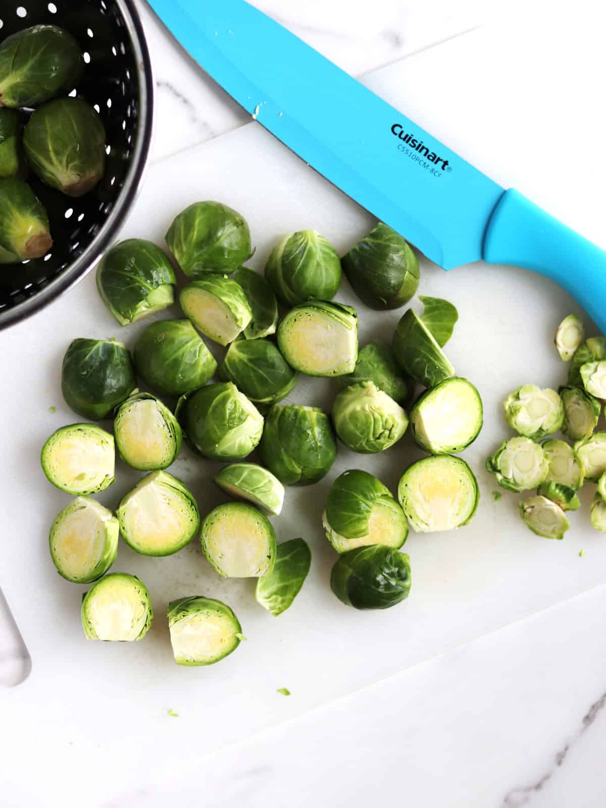 Trimmed and halved fresh Brussels sprouts on a white cutting board.