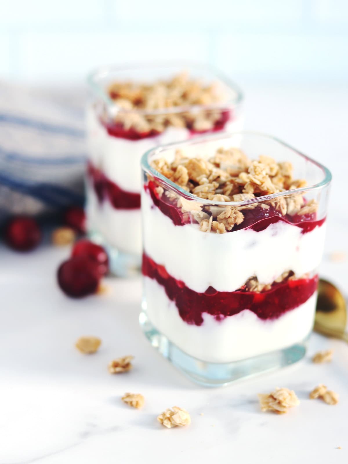 Cranberry yogurt parfaits in glass yogurt jars on a white marble countertop.