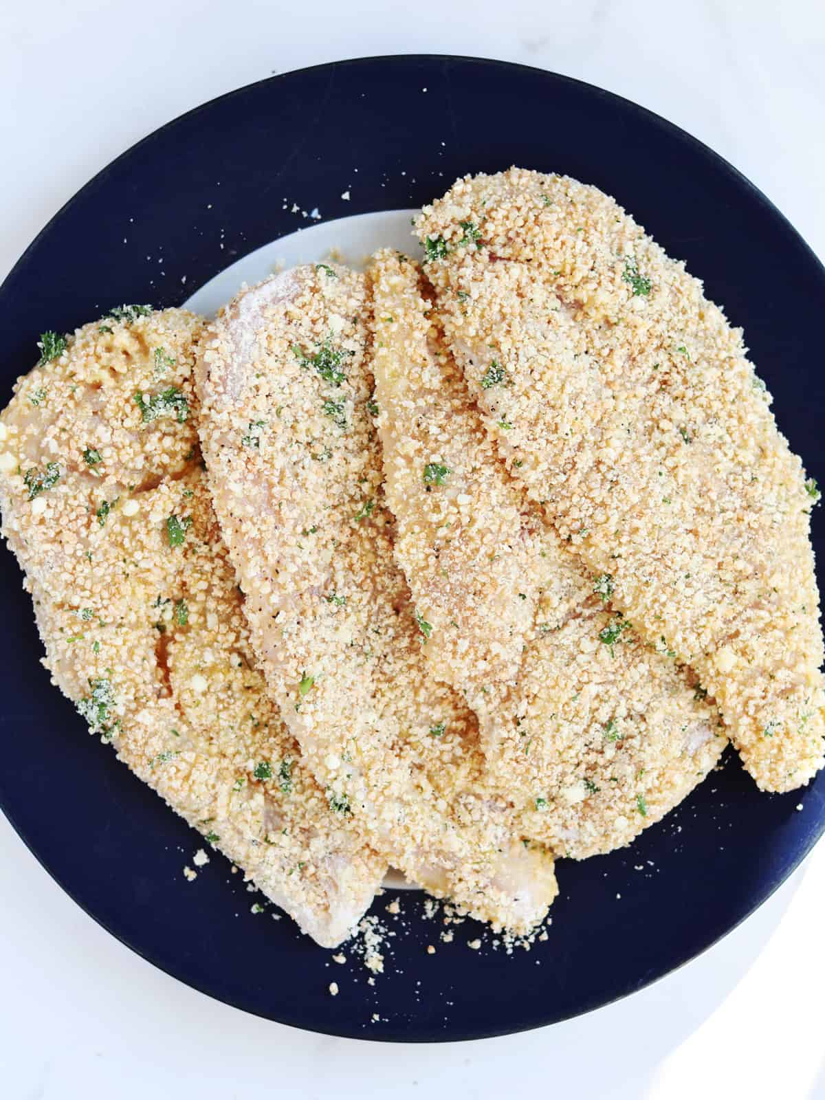 Breaded thin chicken breasts on a blue and white plate.
