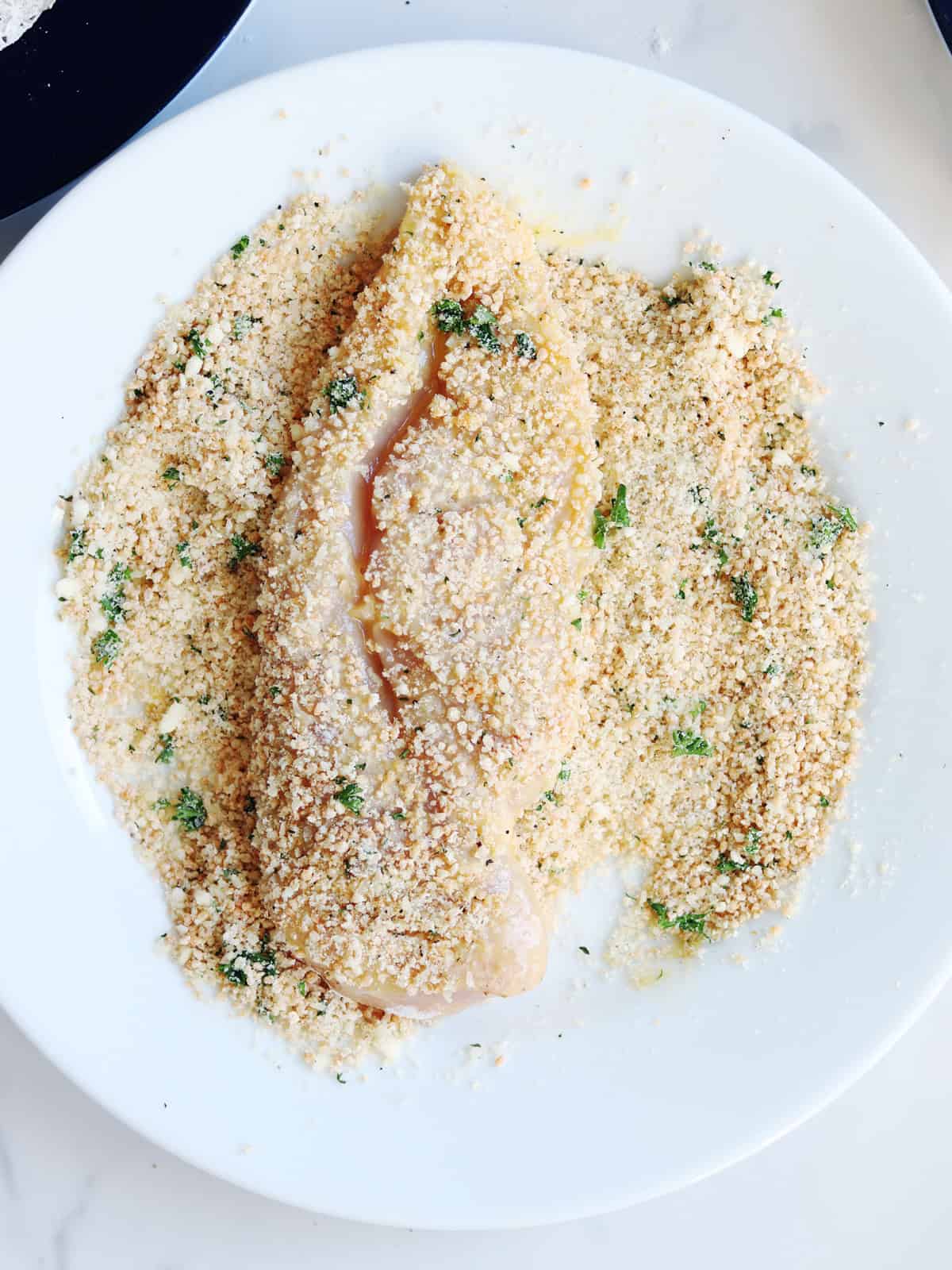 Breaded chicken breast resting on a breadcrumb coated plate.