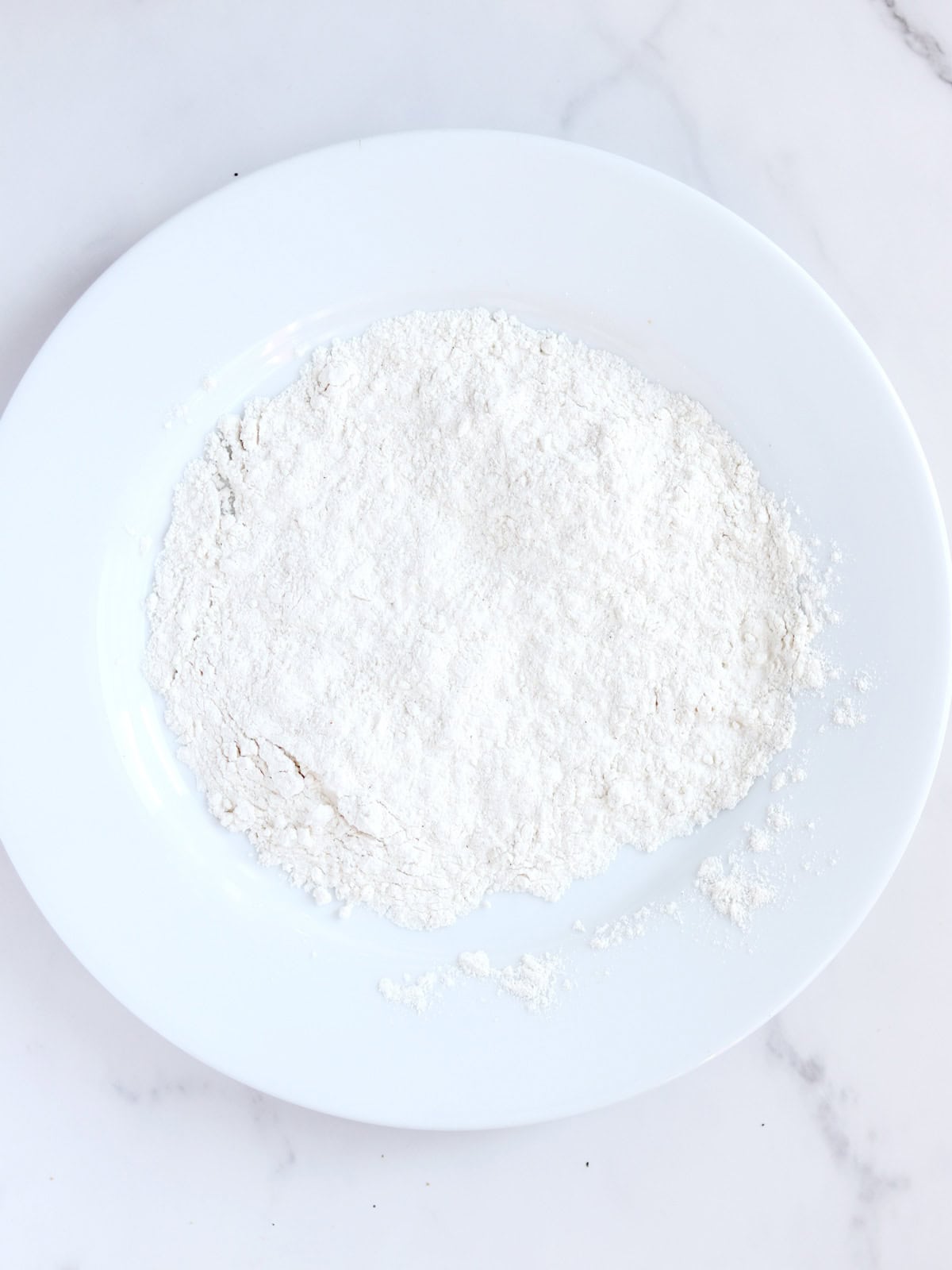 White flour for dredging chicken on a white plate.