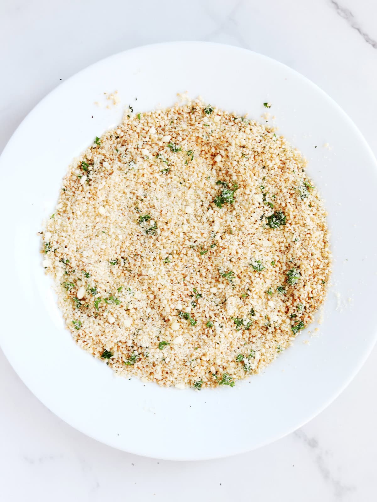 Grated Parmesan and seasoned breadcrumb mixture on a white plate.