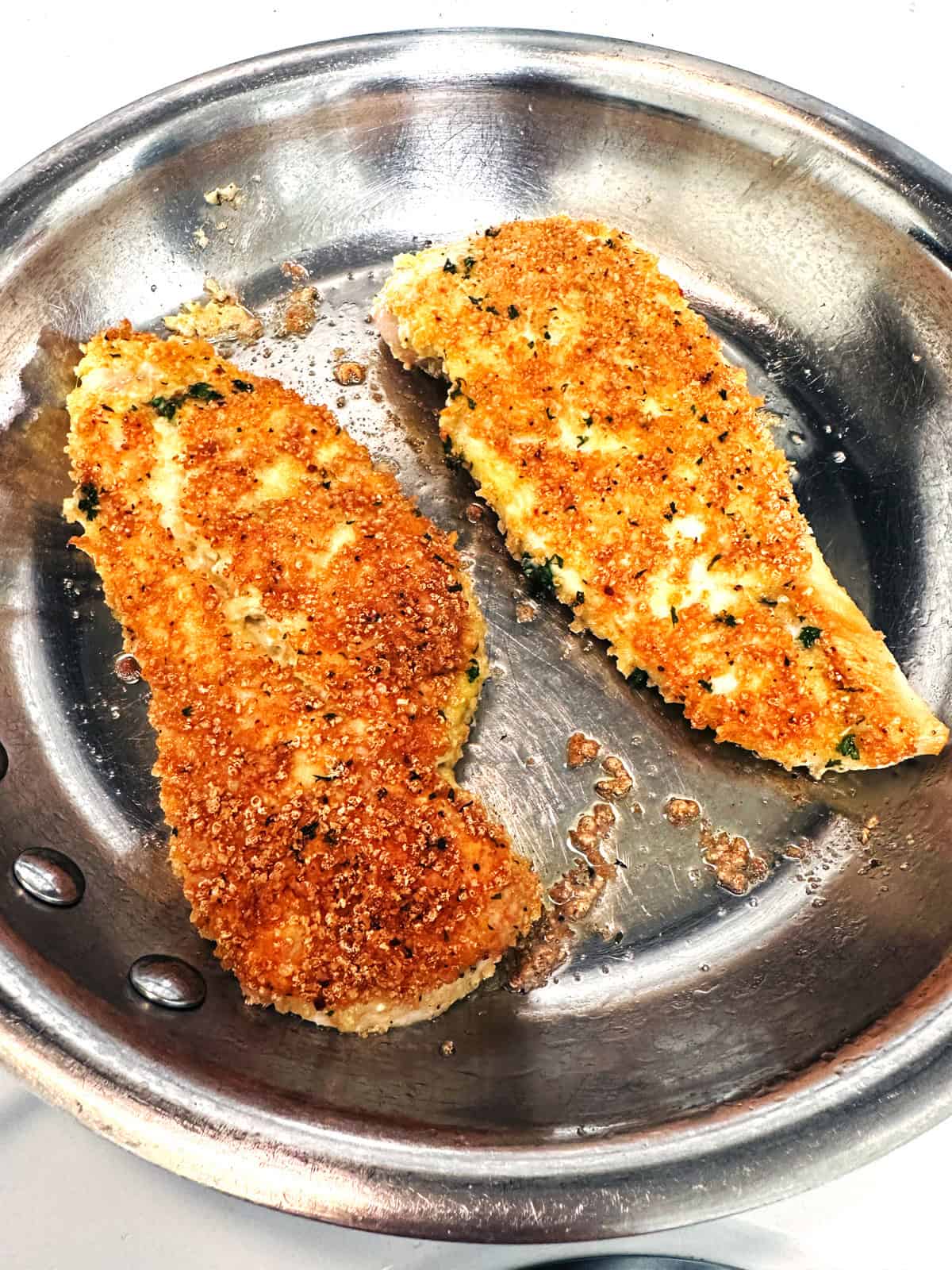 Parmesan breaded chicken breasts in a stainless steel skillet.
