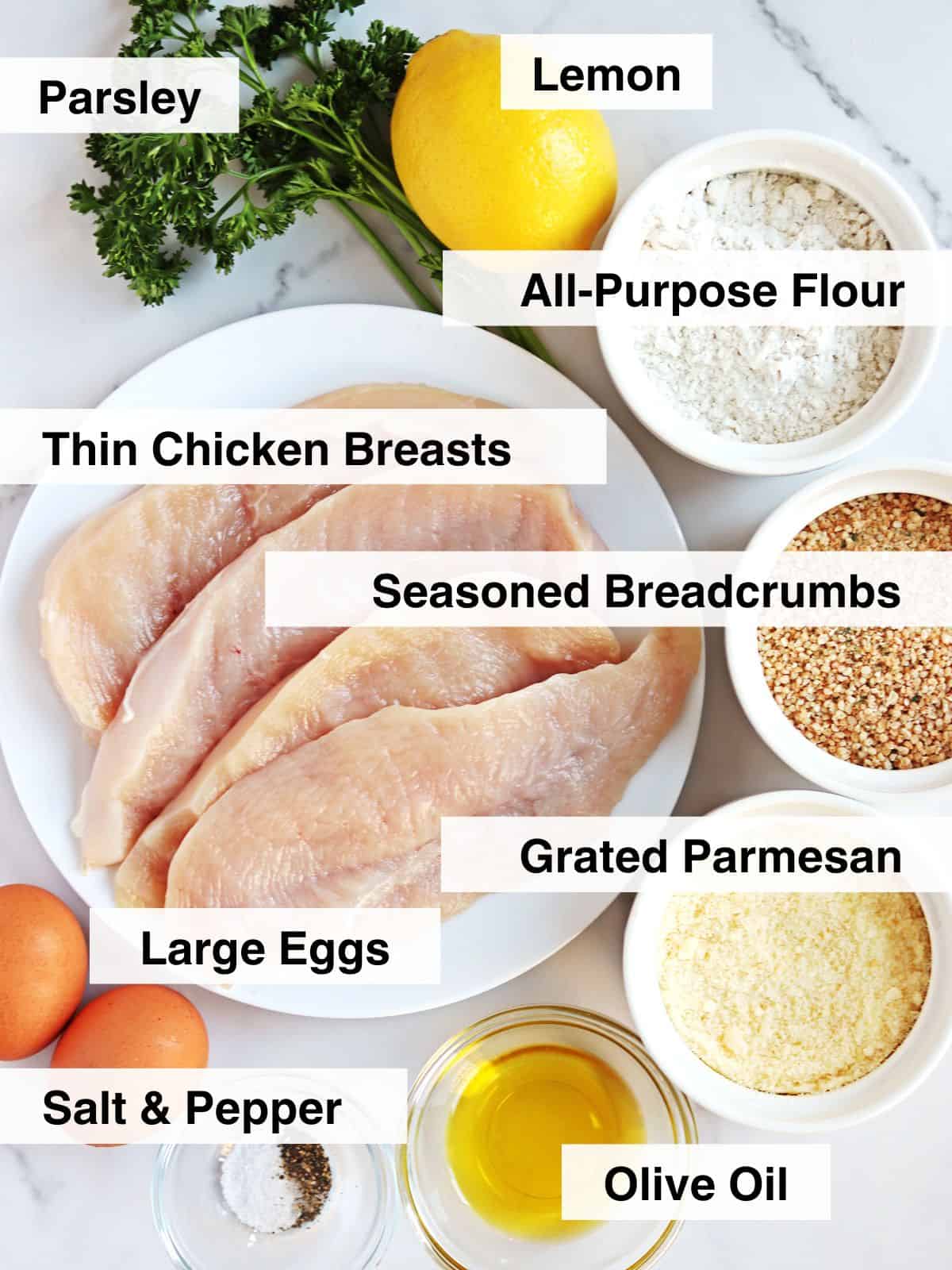 Ingredients for Parmesan crusted chicken arranged on a white marble countertop.
