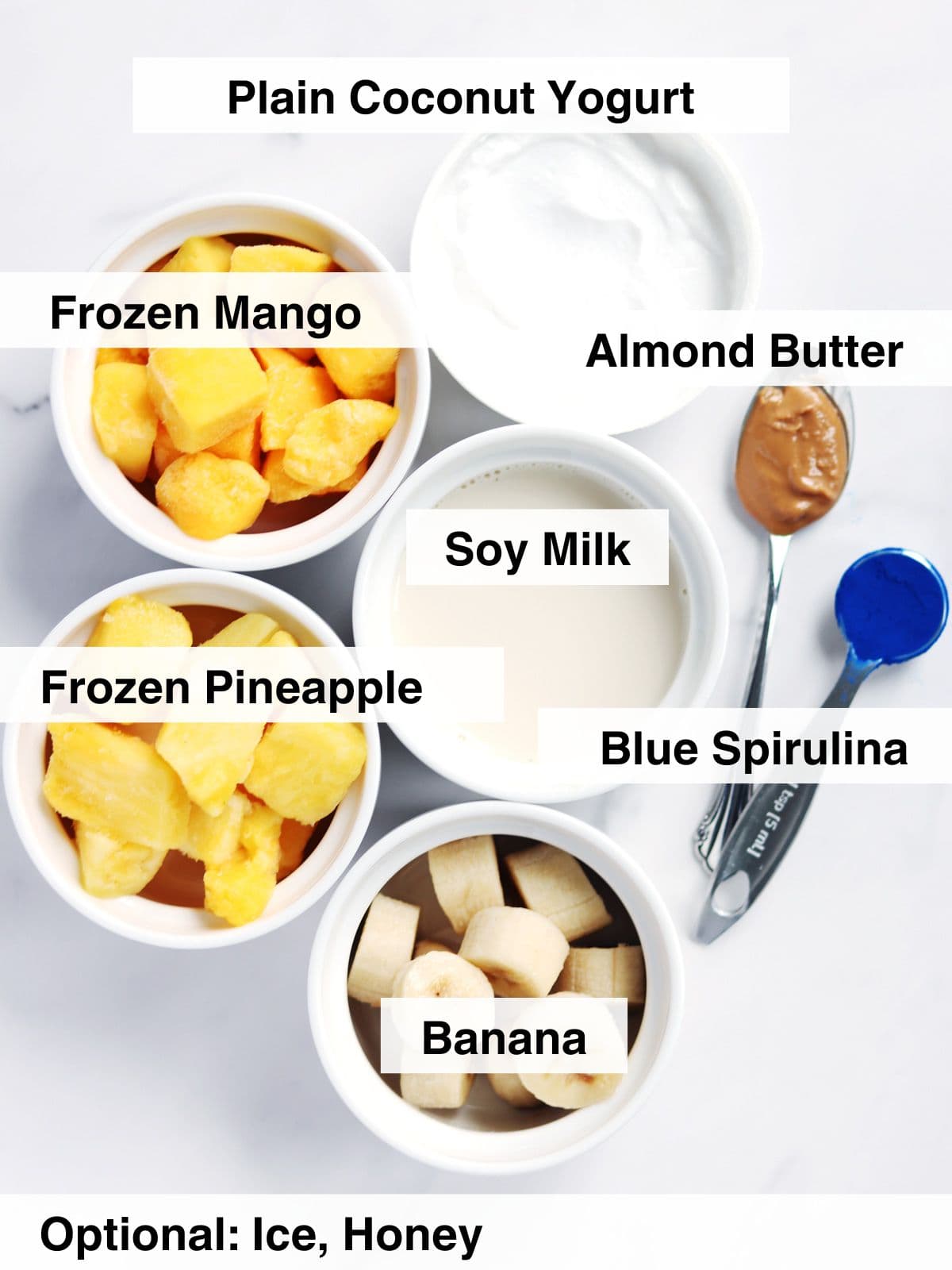 Ingredients for blue spirulina smoothies arranged on a white marble countertop.
