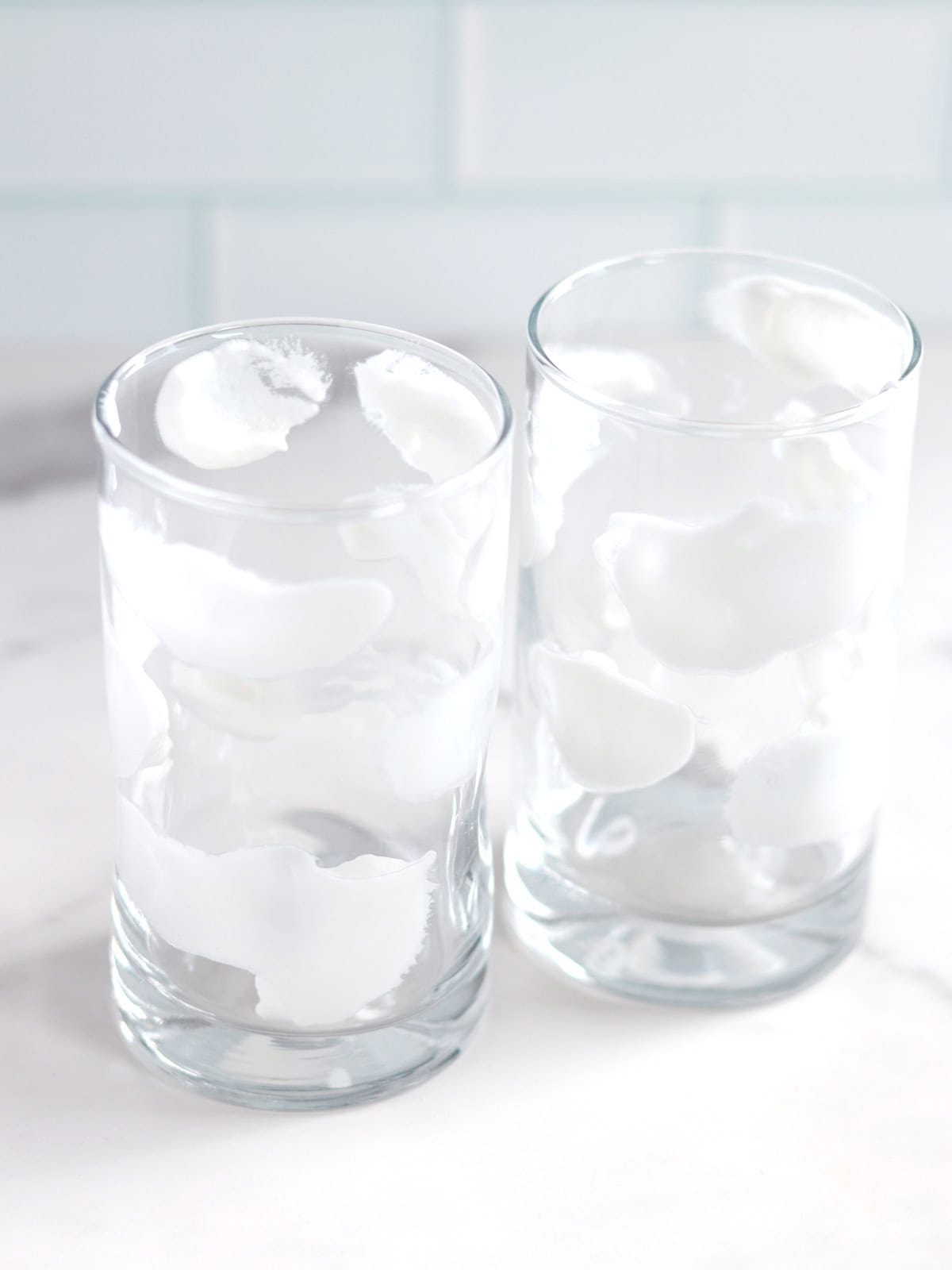 Coconut yogurt "clouds" painted on the sides of two small smoothie glasses.