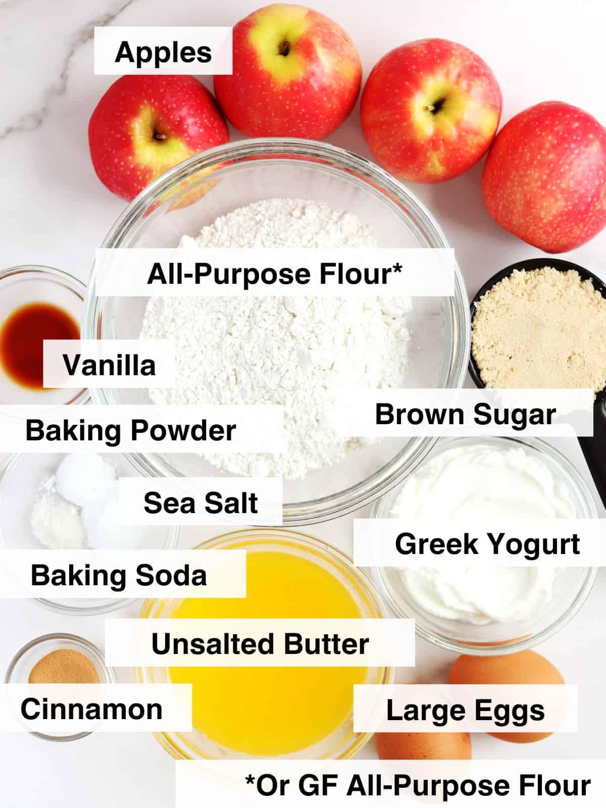 Ingredients for apple muffins arranged on a white marble countertop.