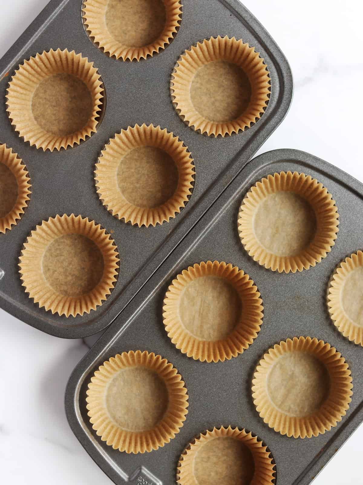 Stainless steel muffin tins prepared with parchment paper liners.