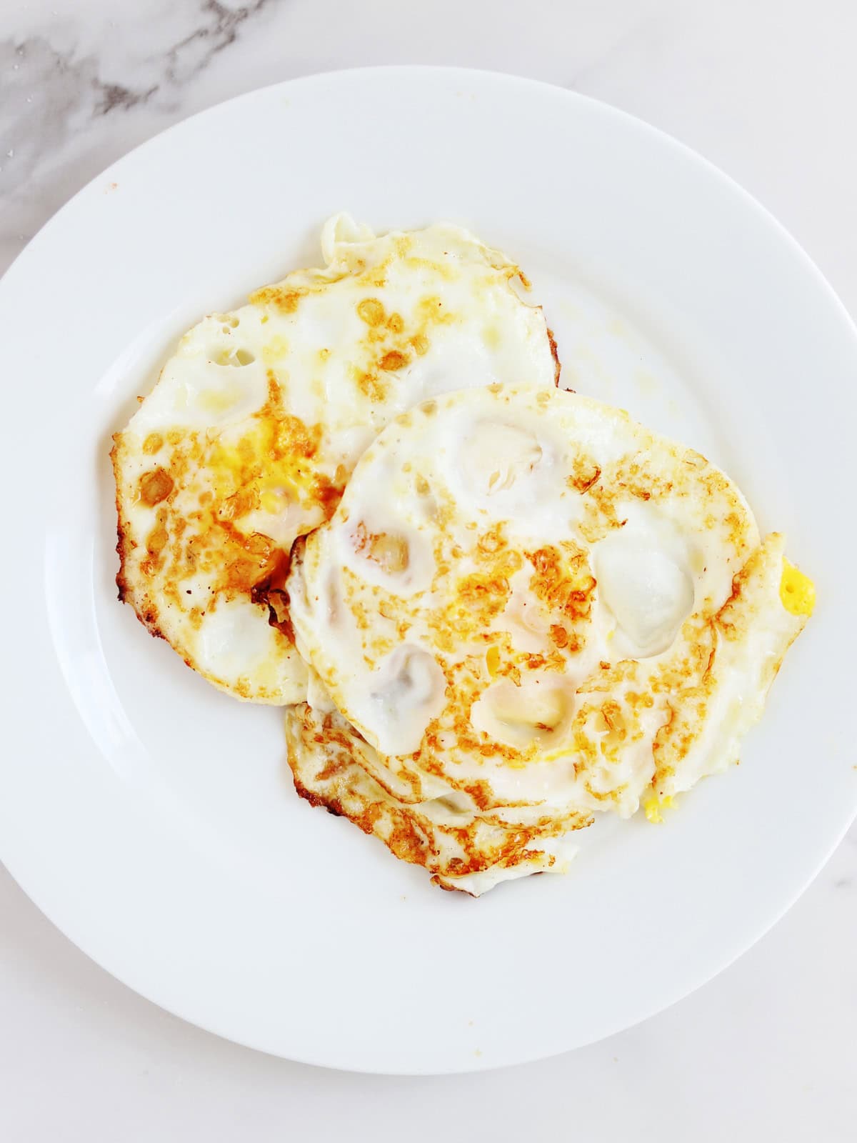 Two fried eggs on a white plate.
