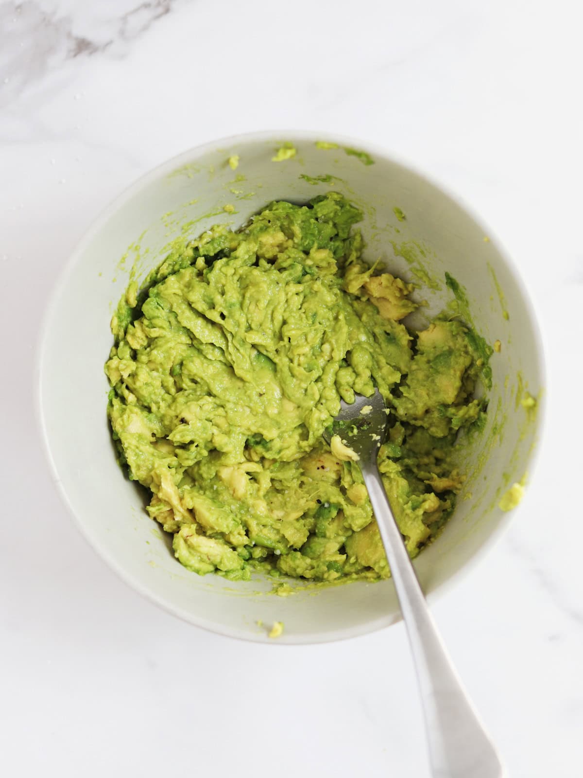 Mashed avocado in a tan ceramic bowl.