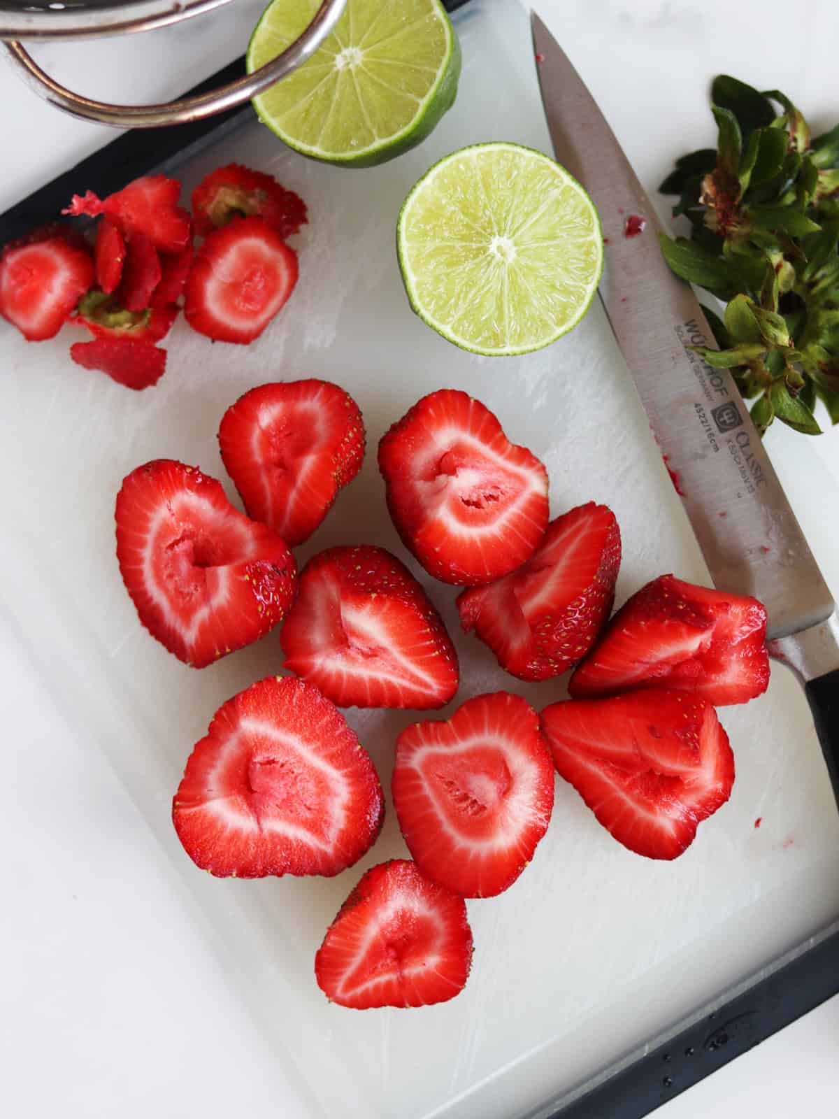 Sliced strawberries and lime on a white and black cutting board.