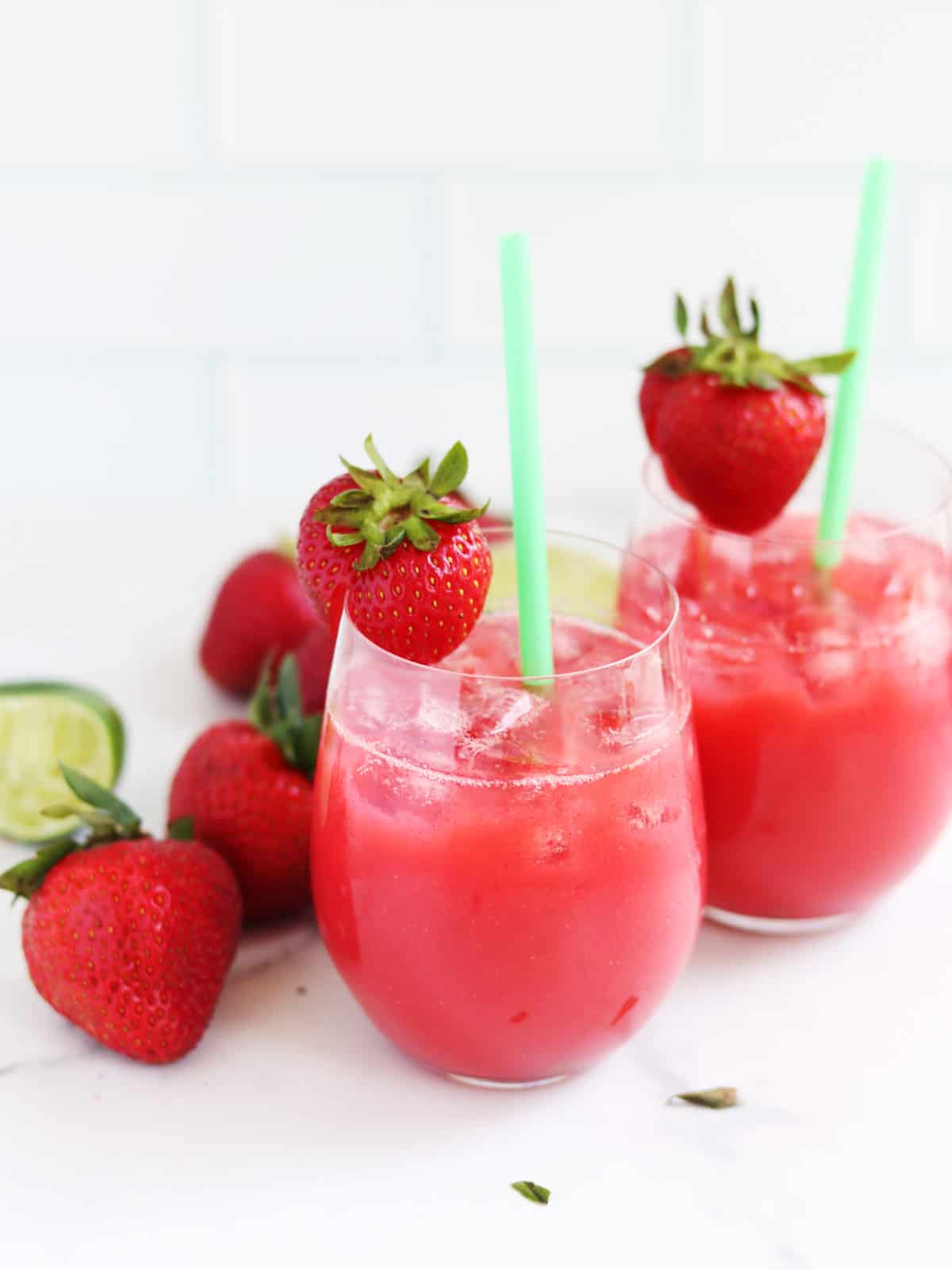 Two strawberry aguas frescas with straws on a white marble countertop.