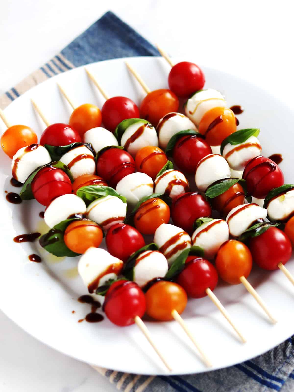 Caprese skewers on a white plate atop a navy and tan plaid napkin.