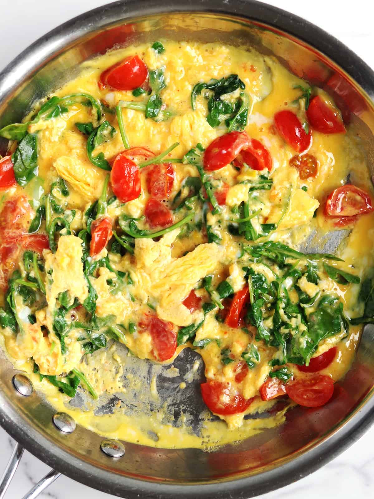 Eggs, arugula and tomatoes cooking in a skillet.
