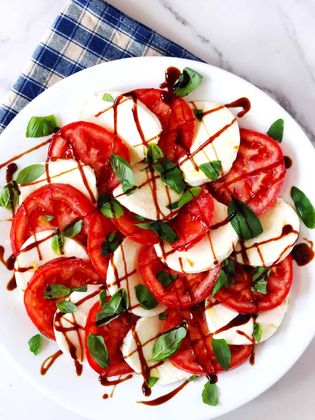 Caprese salad on a white serving plate atop a marble countertop.