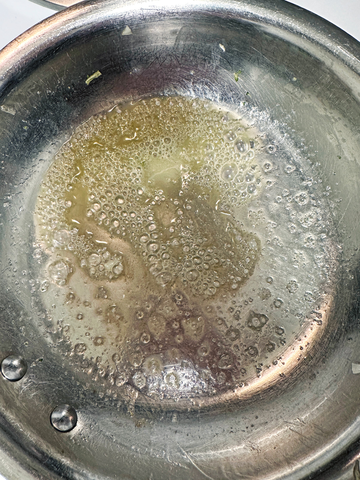 A close-up of a stainless steel pan with melted butter bubbling and sizzling.