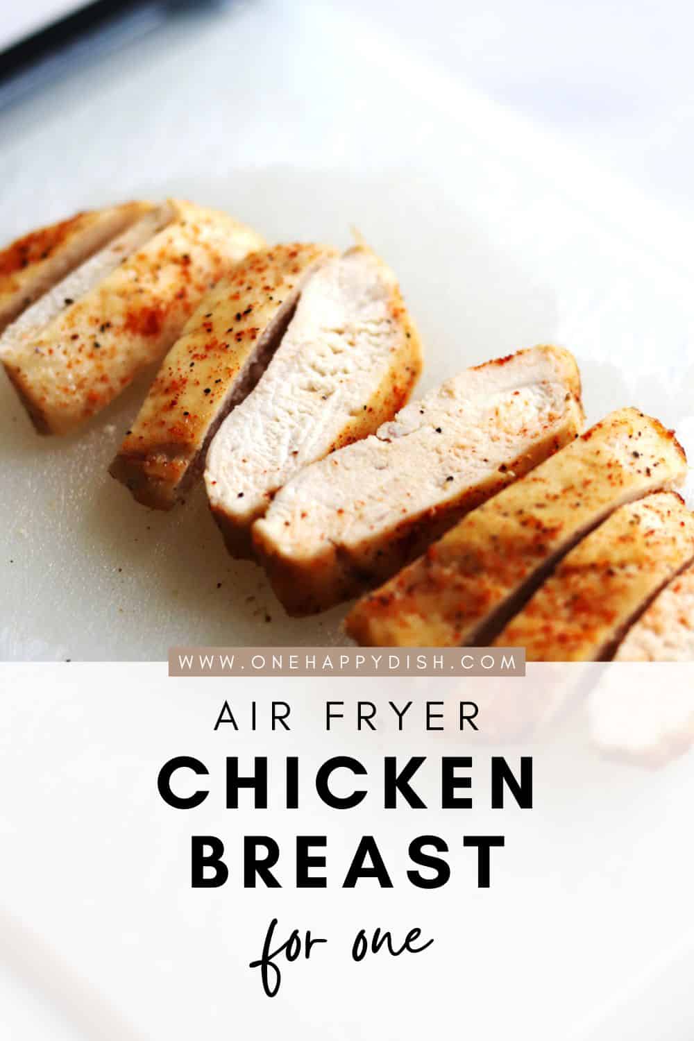 Sliced air fryer chicken breast seasoned with spices on a white cutting board, with text overlay reading Air Fryer Chicken Breast for One and the website onehappydish.com.