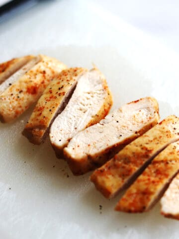 Sliced, cooked air fryer chicken breast seasoned with spices is arranged on a white cutting board. The chicken looks juicy and tender with a light golden-brown exterior.
